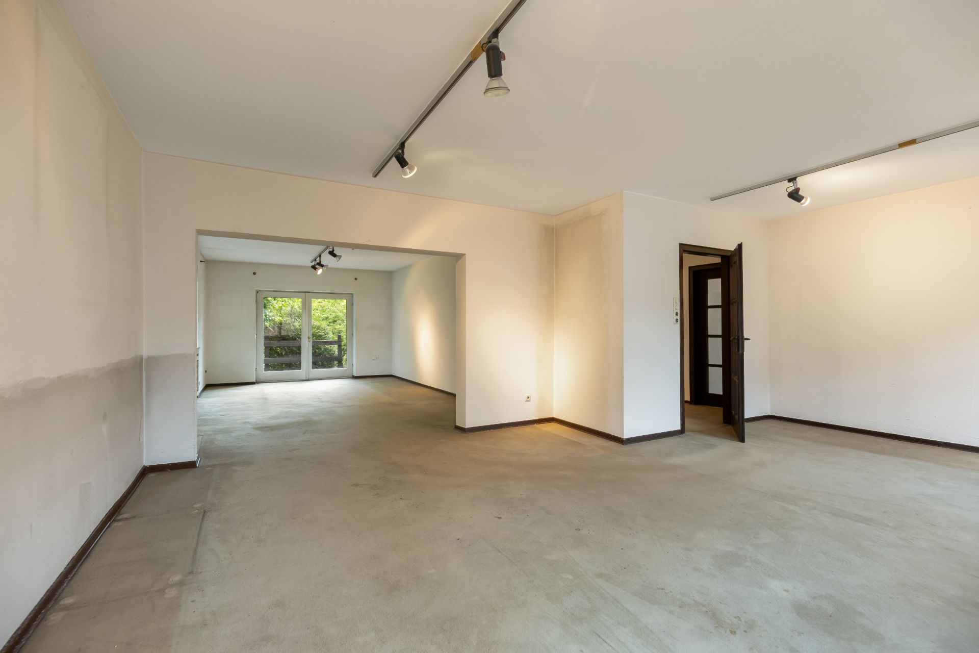 Leerer, großer Wohnraum mit offenen Türen und Blick auf verglaste Terrassentüren im Hintergrund.