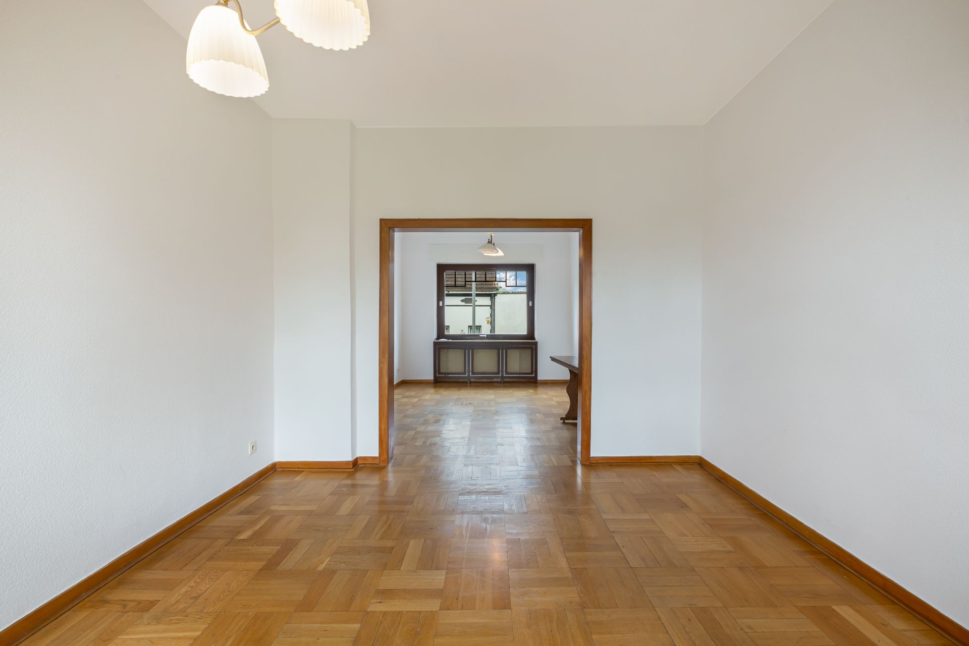 Leerer Raum mit Holzboden, weiß gestrichenen Wänden und zwei Deckenlampen.