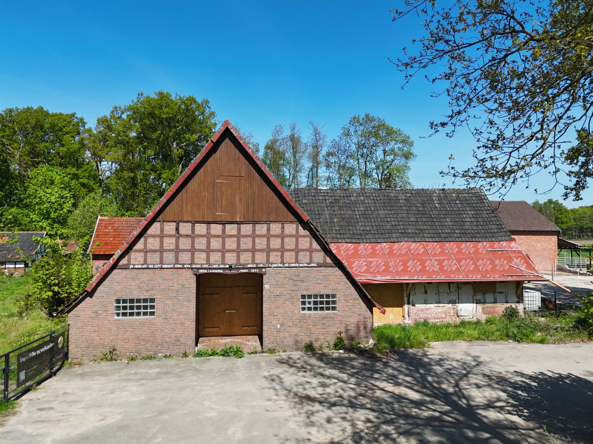 Backstein-Fachwerkhaus mit Satteldach und großem Holztor, umgeben von Bäumen.