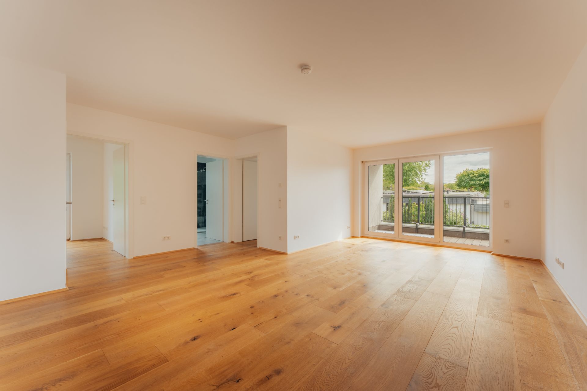 Helles, leeres Wohnzimmer mit Holzboden und großen Fenstern zur Terrasse.