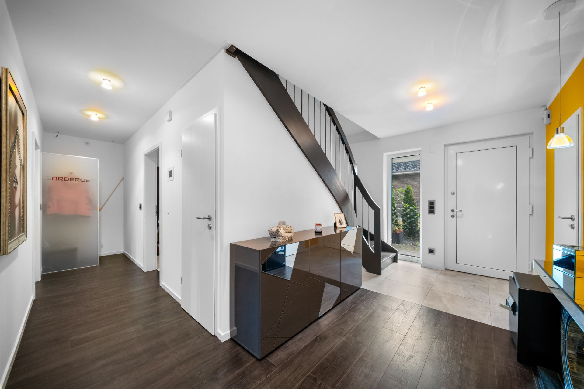 Moderner Flur mit dunklem Boden, weißer Treppe und Türen, Kommode und Spiegel.