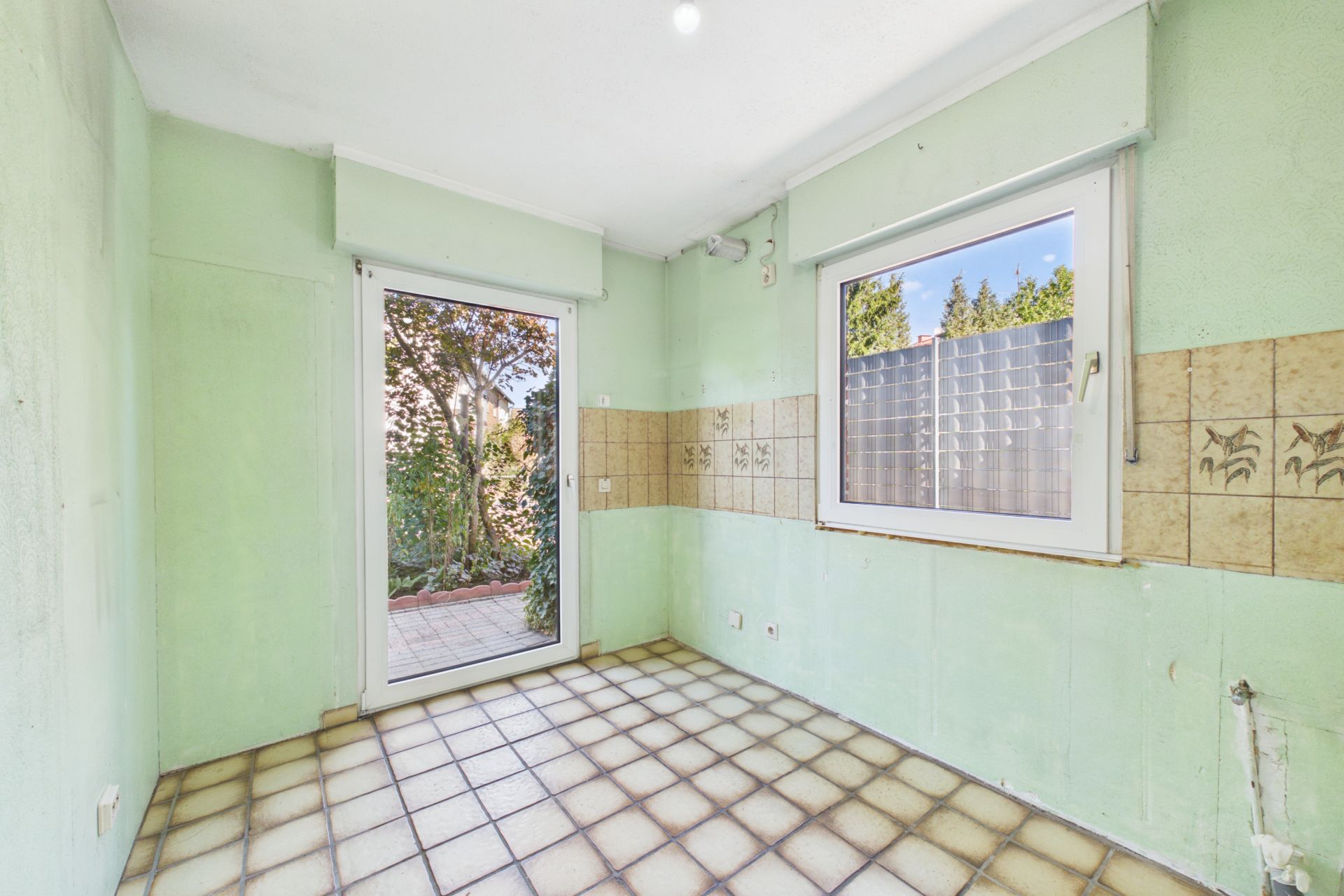 Leerer Raum mit Fliesenboden, grün gestrichenen Wänden, Fenster und Tür zum Garten.