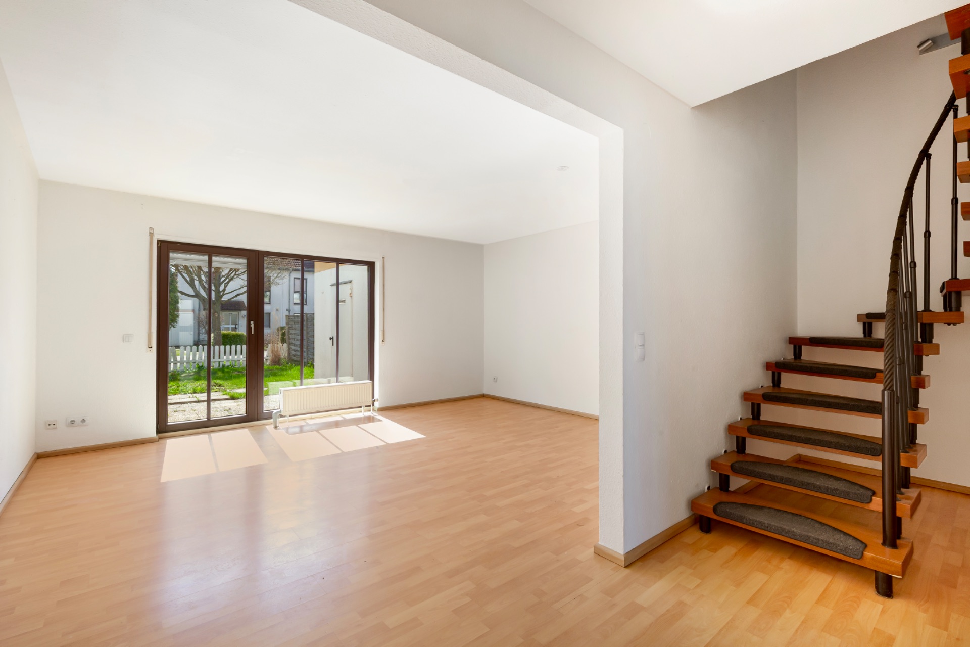 Helles Wohnzimmer mit Holzfußboden, großer Glastür zum Garten und offener Holztreppe.