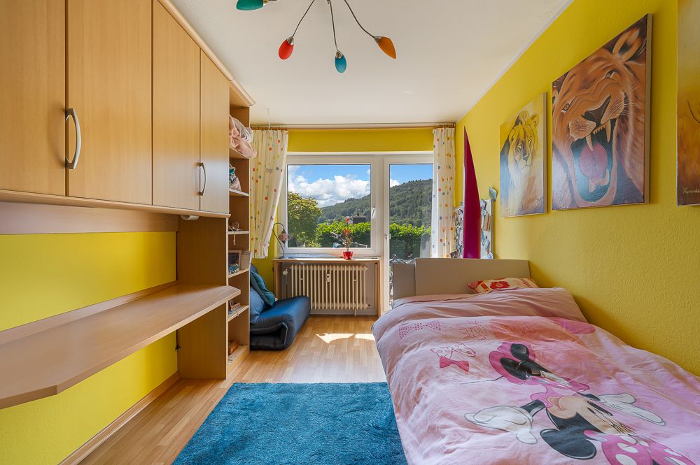Helles Kinderzimmer mit gelben Wänden, Einzelbett, Schreibtisch, Regalen und Tierbildern an der Wand.