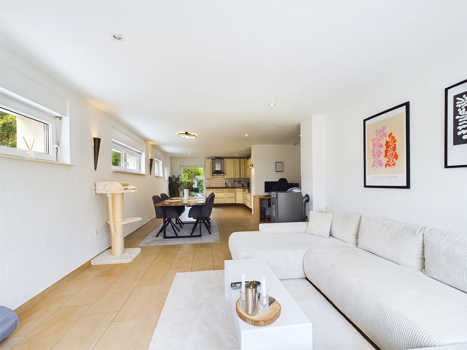 Helles Wohnzimmer mit weißem Sofa, Essbereich, Küchenblick und Kletterbaum für Katzen.
