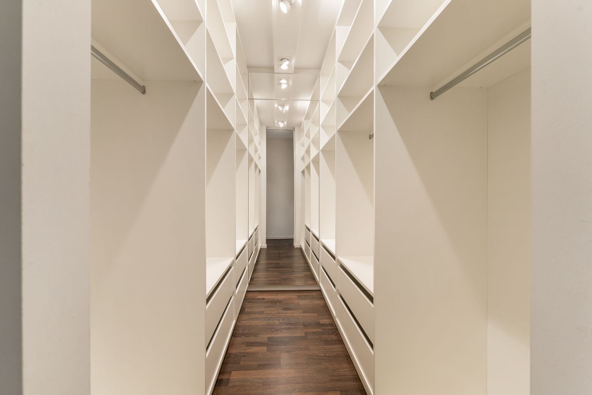 Geräumiger, heller begehbarer Kleiderschrank mit weißen Regalen und dunklem Holzboden.