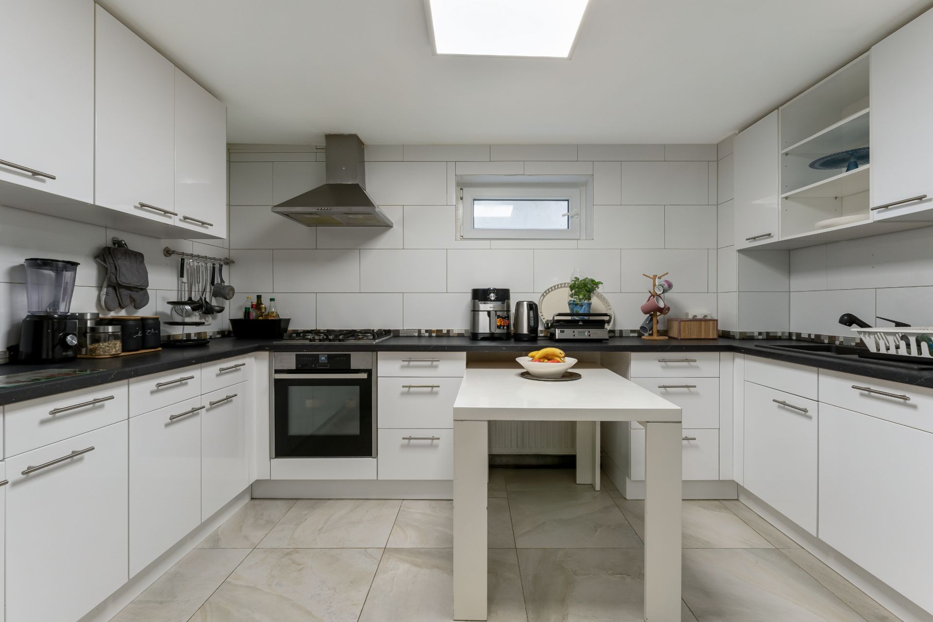 Moderne weiße Einbauküche mit Küchengeräten und Tisch in der Mitte.