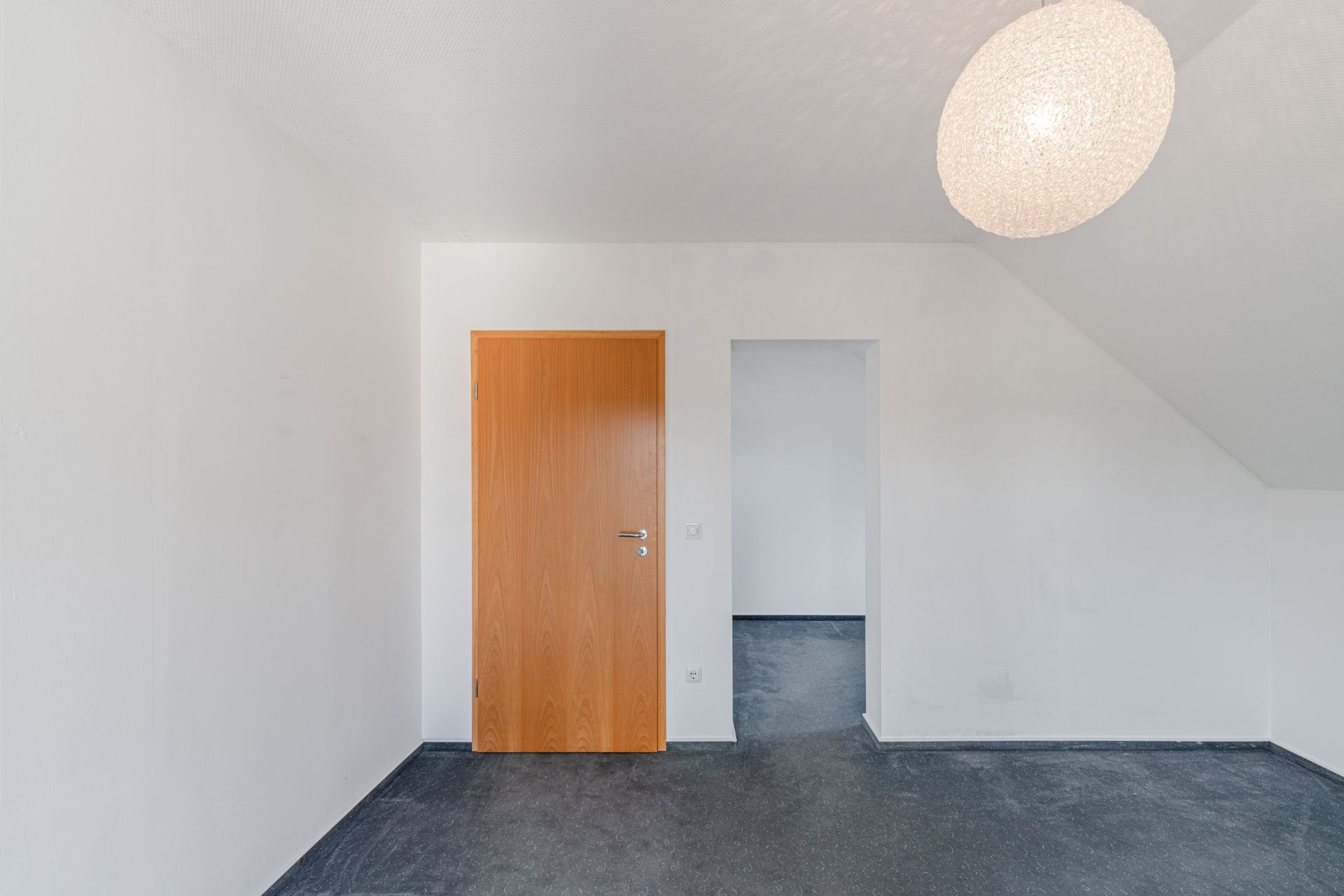Leeres Zimmer mit weißer Wand, Holztür, Durchgang und runder Deckenleuchte.