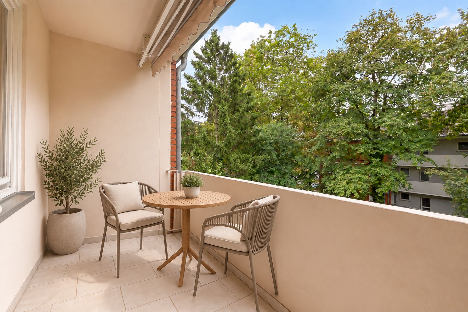Balkon mit zwei Stühlen, einem runden Tisch und Topfpflanzen, Blick auf grüne Bäume.