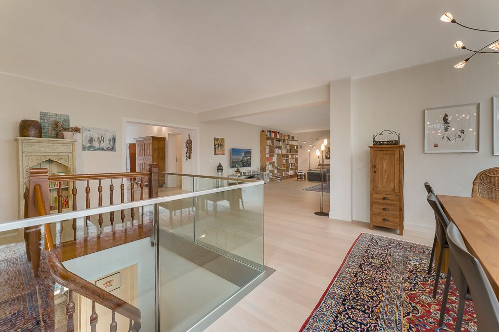Heller Wohnraum mit Treppe, Holzmöbeln, Teppich und Regal mit Büchern.