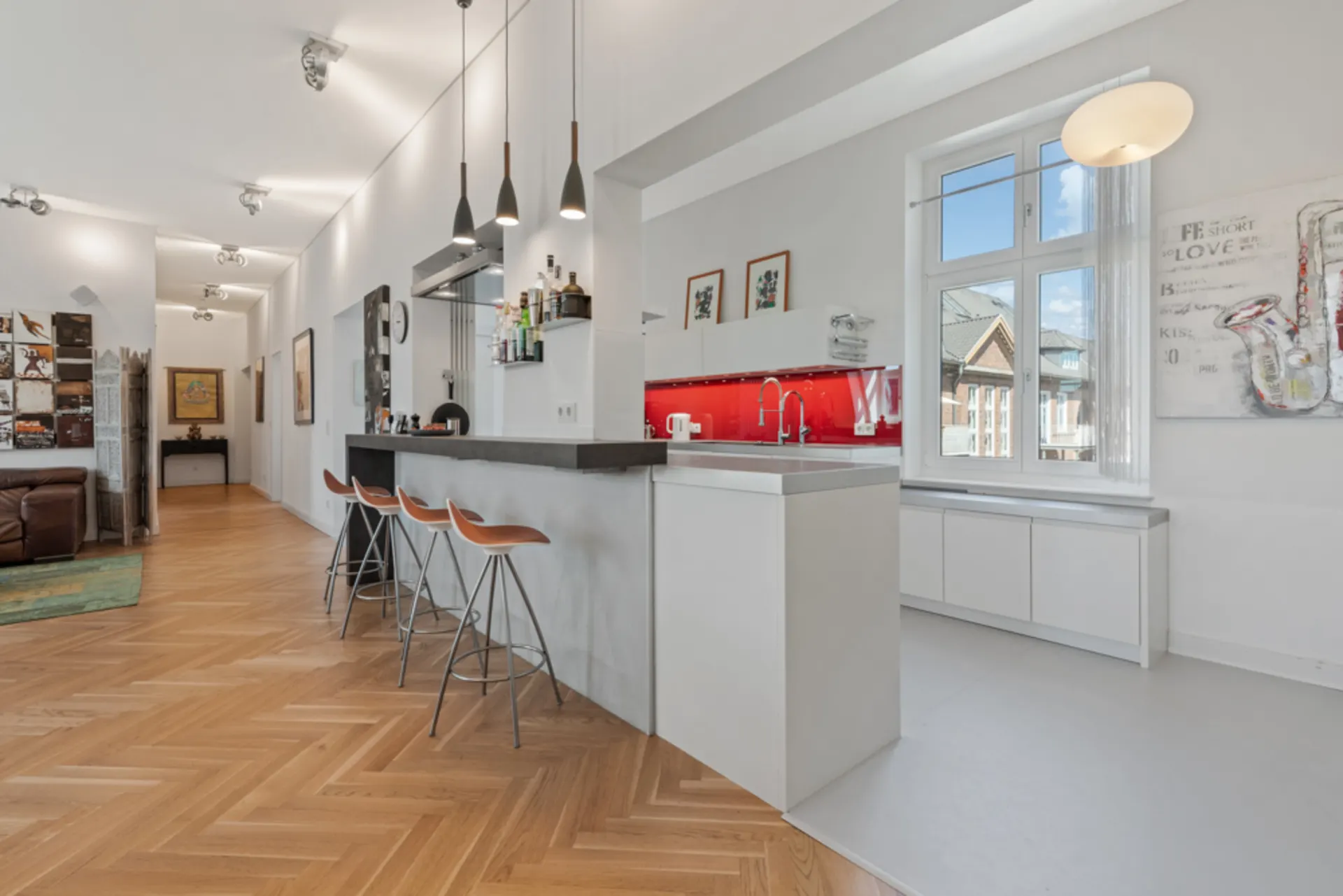 Moderne Küche mit rotem Fliesenspiegel, Bartresen und drei Barhockern, Parkettboden und großem Fenster.
