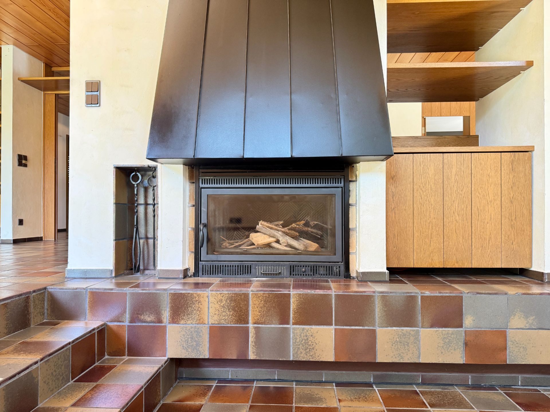 Kamin mit schwarzem Schornstein auf gefliester Stufe und Holzschränken.