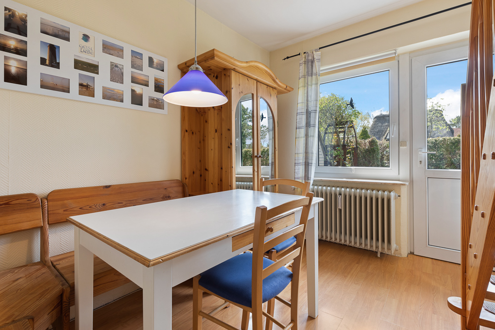 Essbereich mit Holztisch, Stühlen, Eckbank, Fenster, Tür und einer blauen Deckenlampe.