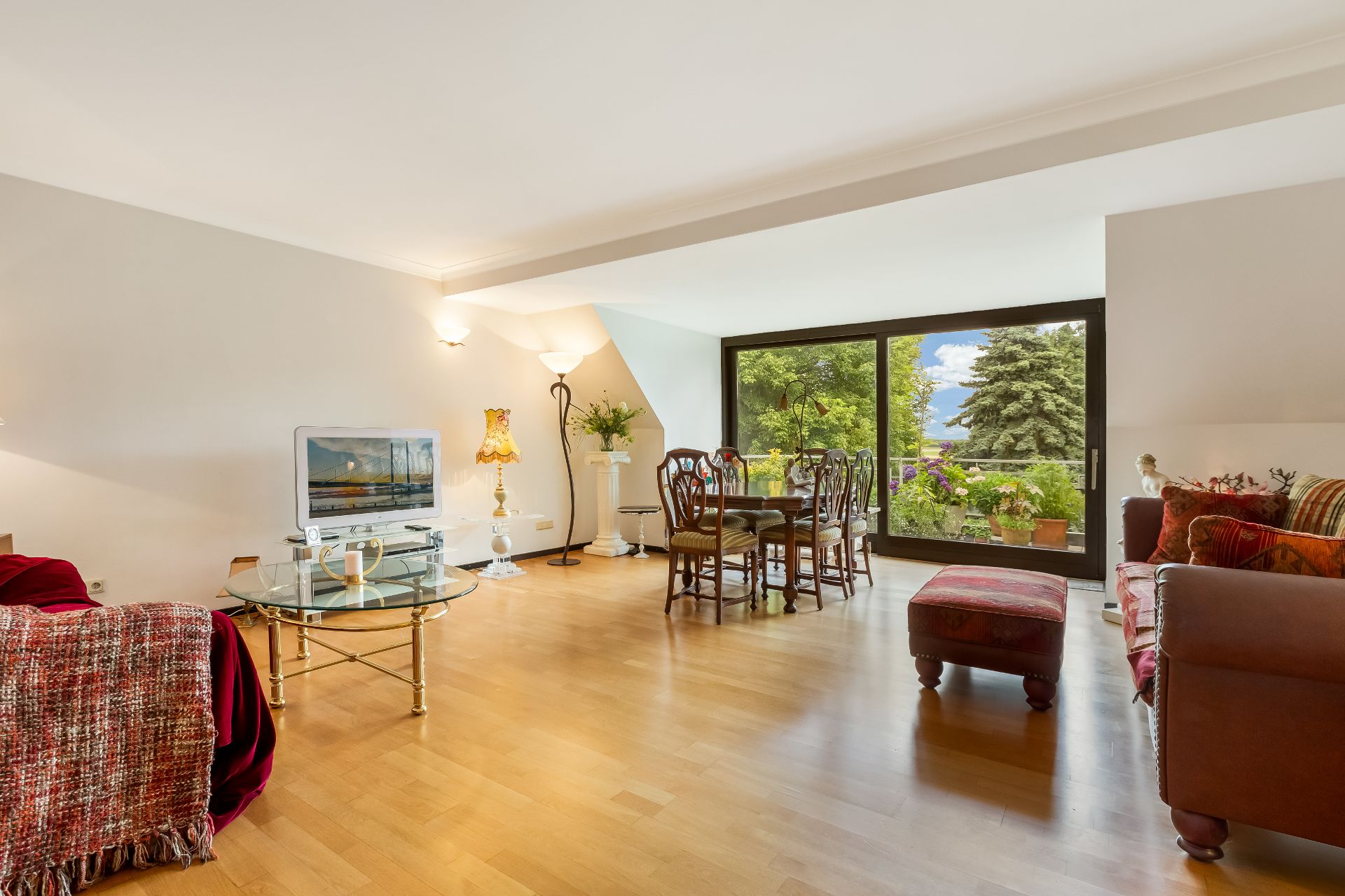 Helles Wohnzimmer mit Holzboden, Essbereich, Sofas und großem Fenster zum Garten.