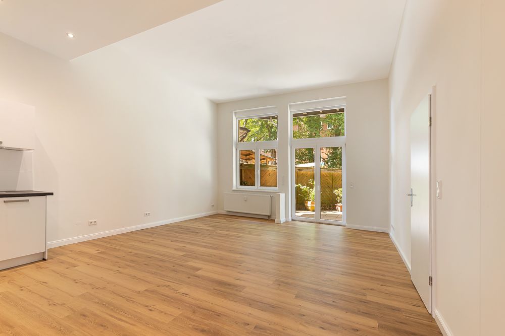 Heller Raum mit Holzfußboden, großen Fenstern und Zugang zu einer Terrasse.