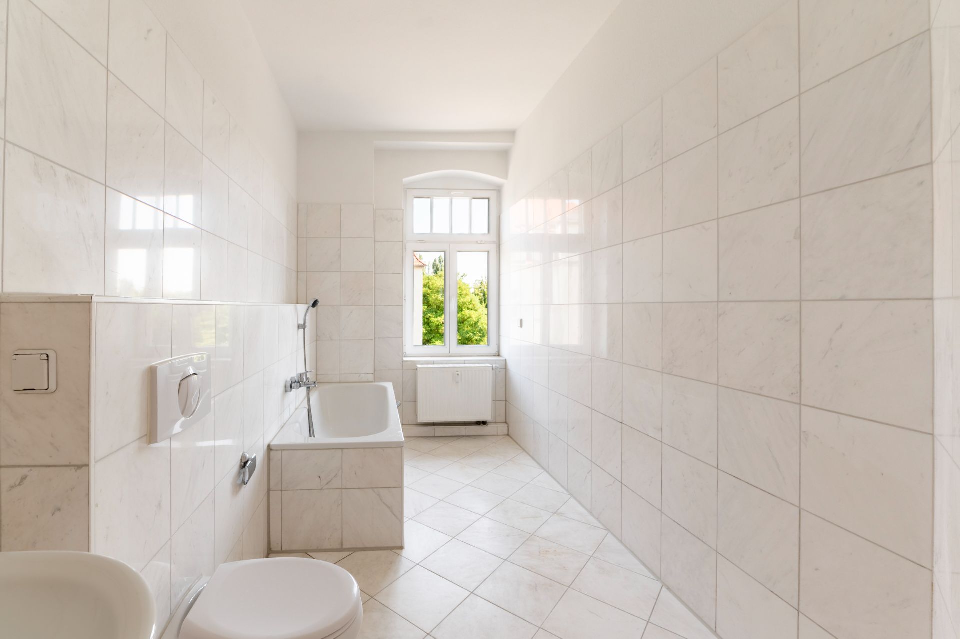 Helles Badezimmer mit Badewanne, Toilette, Fliesenboden und Fenster.