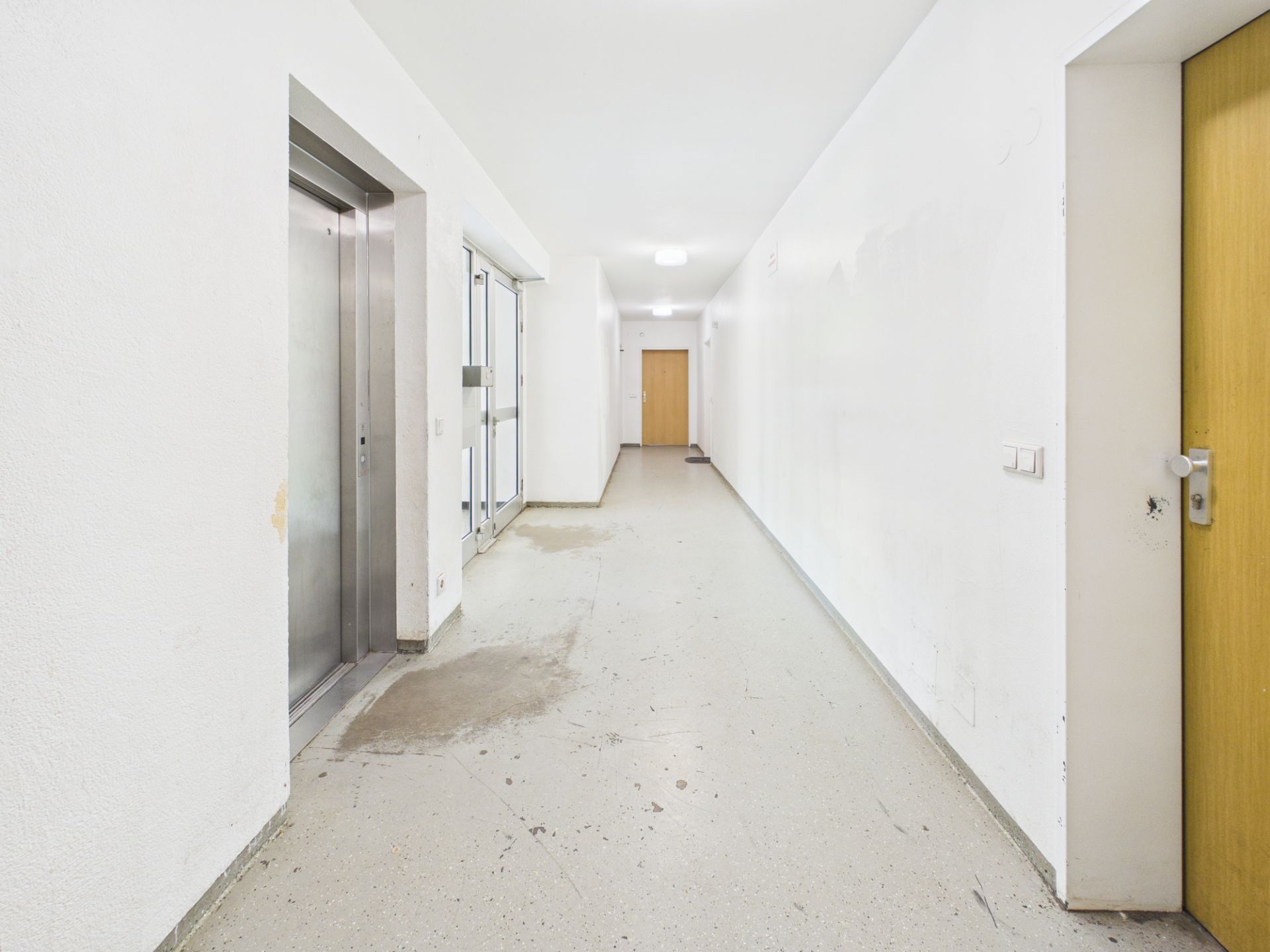 Heller Flur mit Aufzug, Türen und Fenstern in einem Wohngebäude.