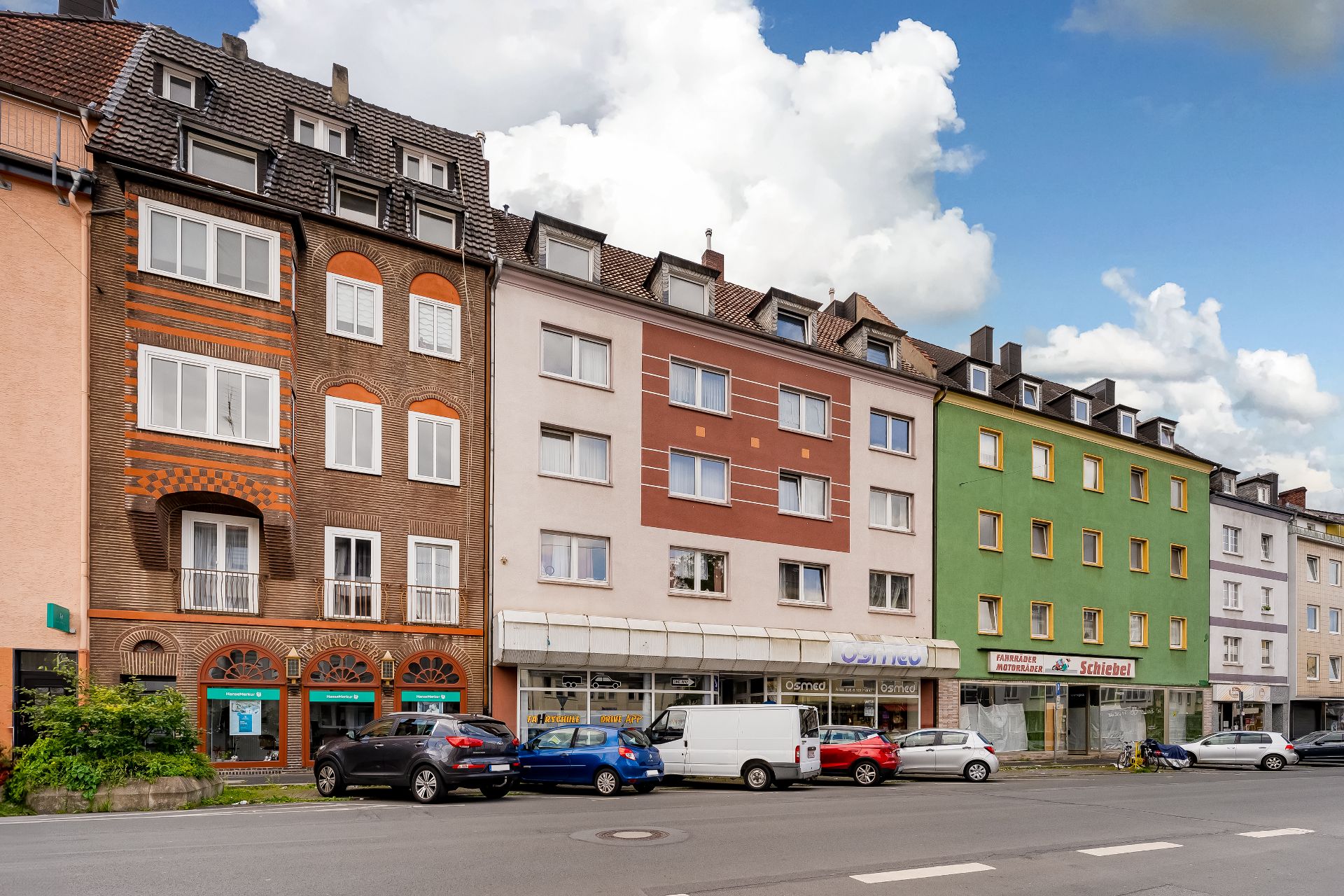 Mehrere Wohngebäude mit Geschäften im Erdgeschoss und Autos auf der Straße davor.