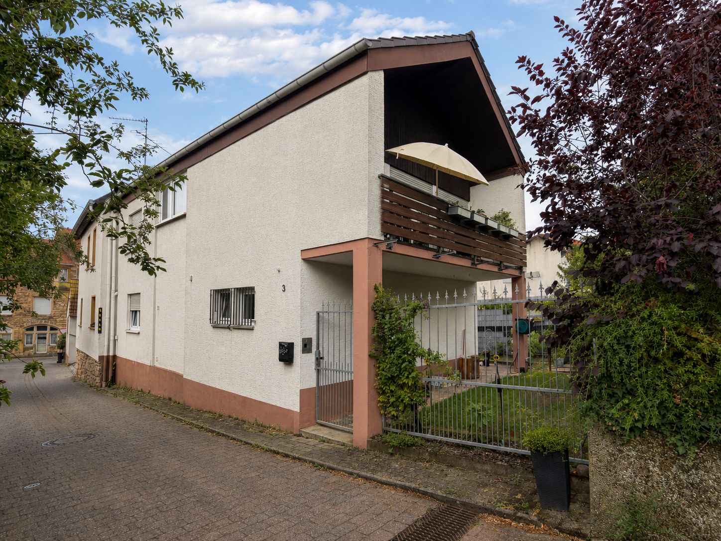 Zweistöckiges Wohnhaus mit Balkon und kleinem Garten, Zaun vor dem Haus.