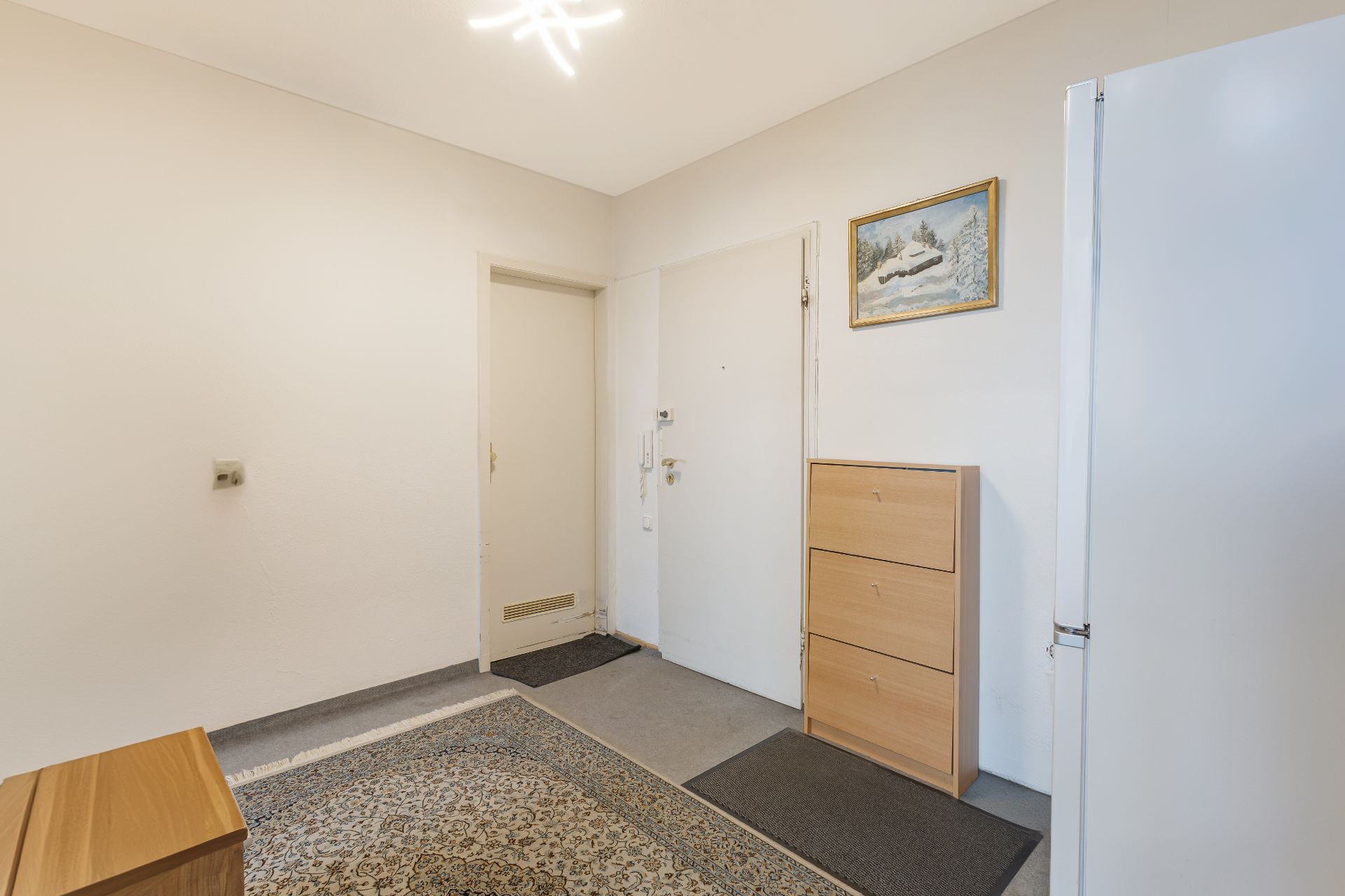 Heller Flur mit Teppich, Schuhschrank, weißer Tür und Wandbild.