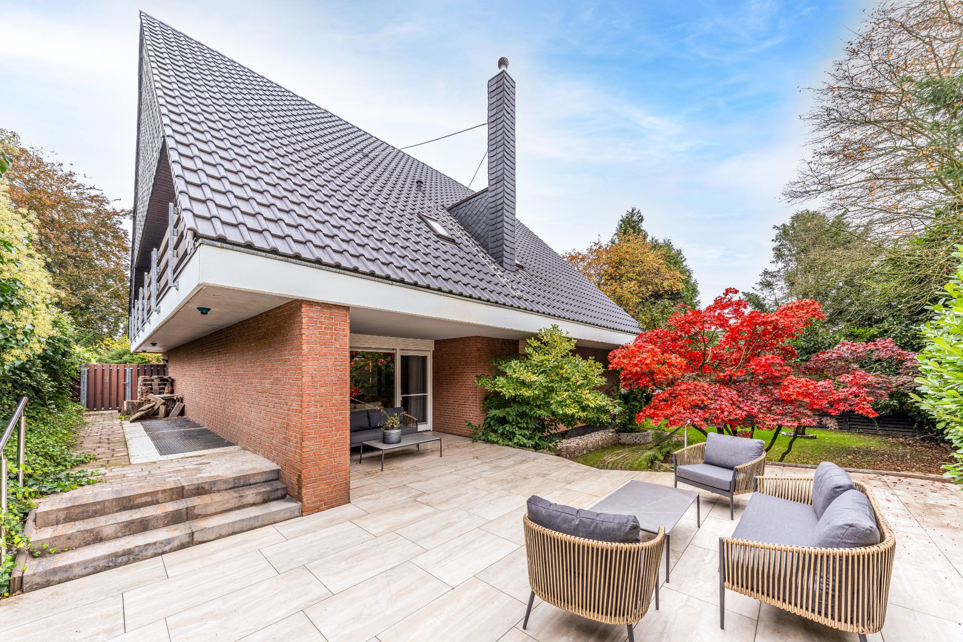 Moderne Terrasse mit Sitzmöbeln, großem Dach und Garten mit rotem Baum.