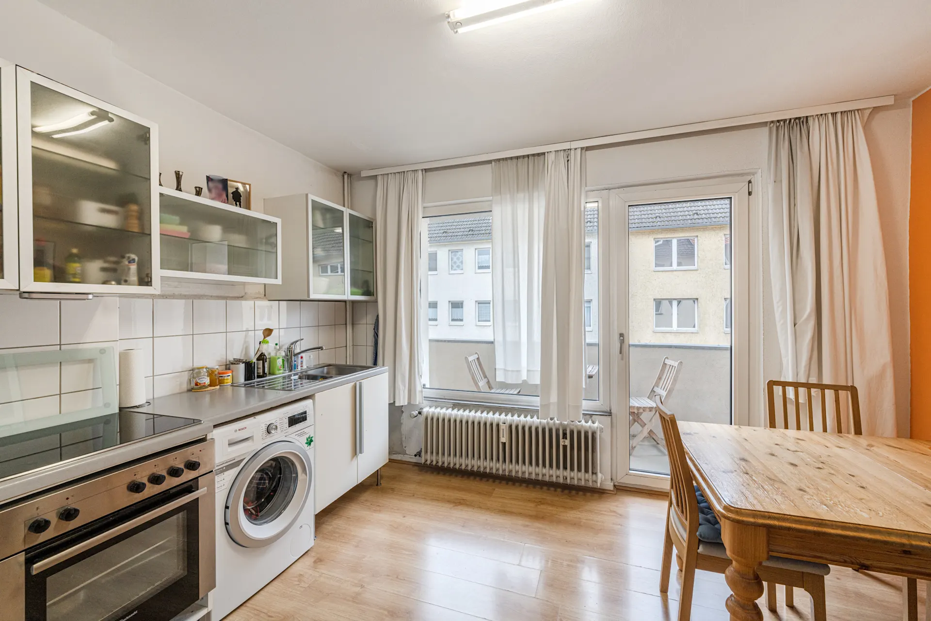 Helle Küche mit Esstisch, Herd, Waschmaschine und Zugang zu einem Balkon mit Stühlen.