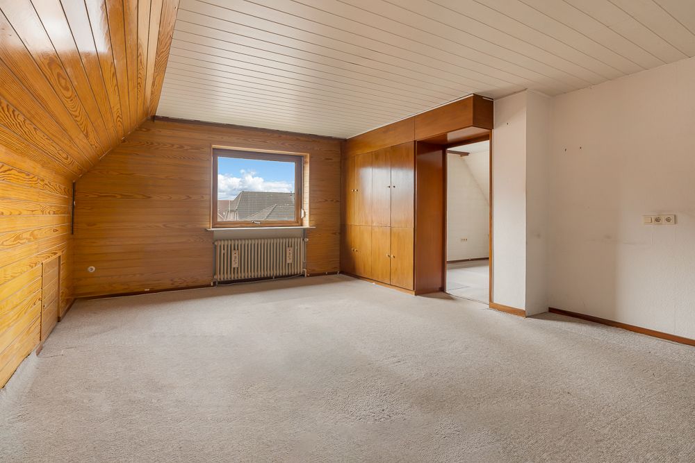 Leeres Zimmer mit Holzvertäfelung, Fenster, Heizkörper und Einbauschrank.