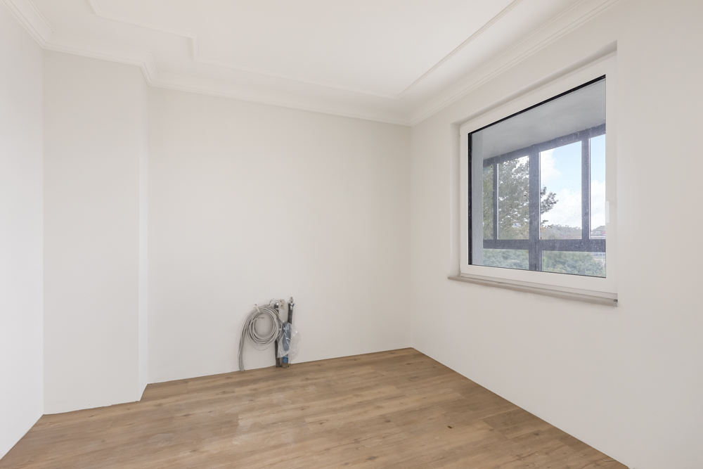 Leerer Raum mit weißer Wand, großem Fenster und Holzboden, Kabel an der Wand.