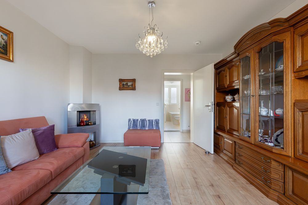 Wohnzimmer mit Sofa, Kamin, Glastisch und Holzvitrine, Tür zum anderen Raum offen.