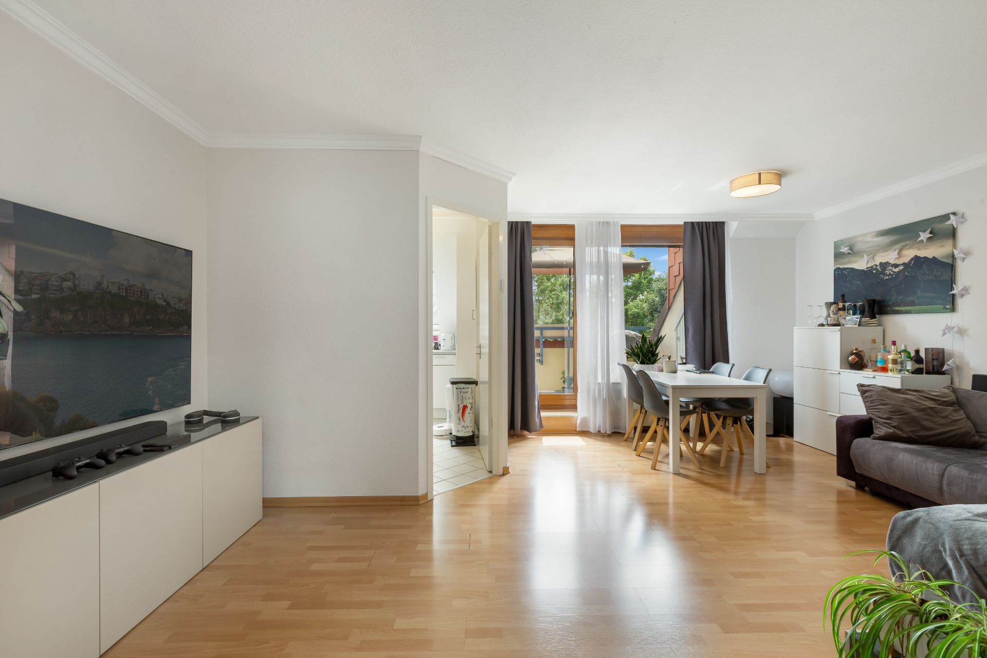 Modernes Wohnzimmer mit Holzboden, Sofa, Esstisch, Fenster und Fernseher.