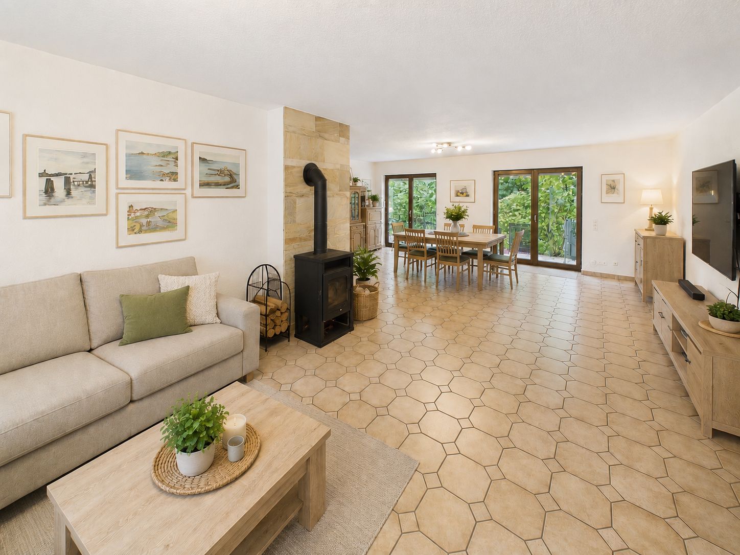 Helles Wohnzimmer mit Sofa, Holztisch, Kaminofen und Essbereich mit großem Fenster.