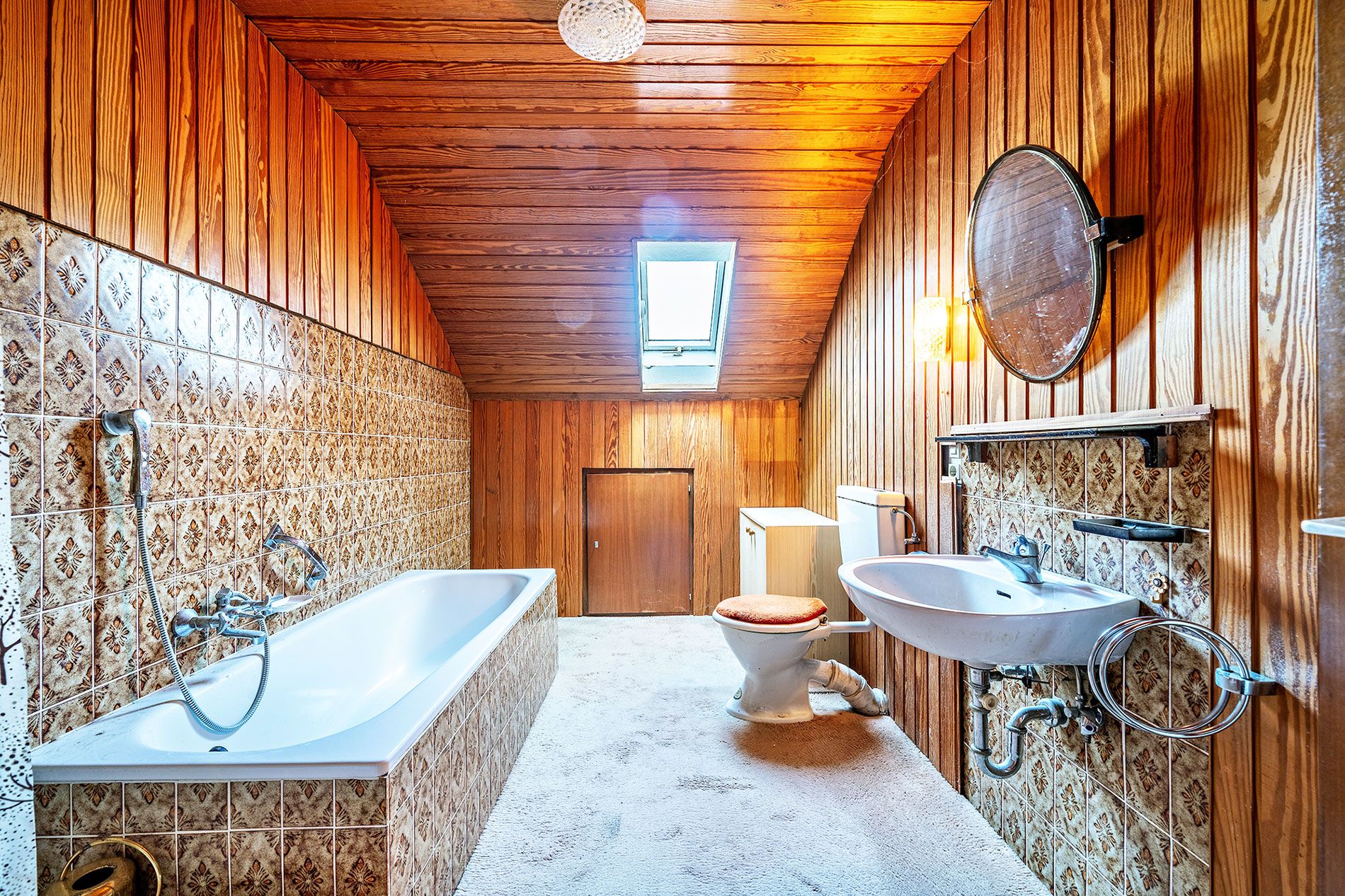Badezimmer mit Badewanne, Waschbecken, WC und Holzvertäfelung unter dem Dachfenster.