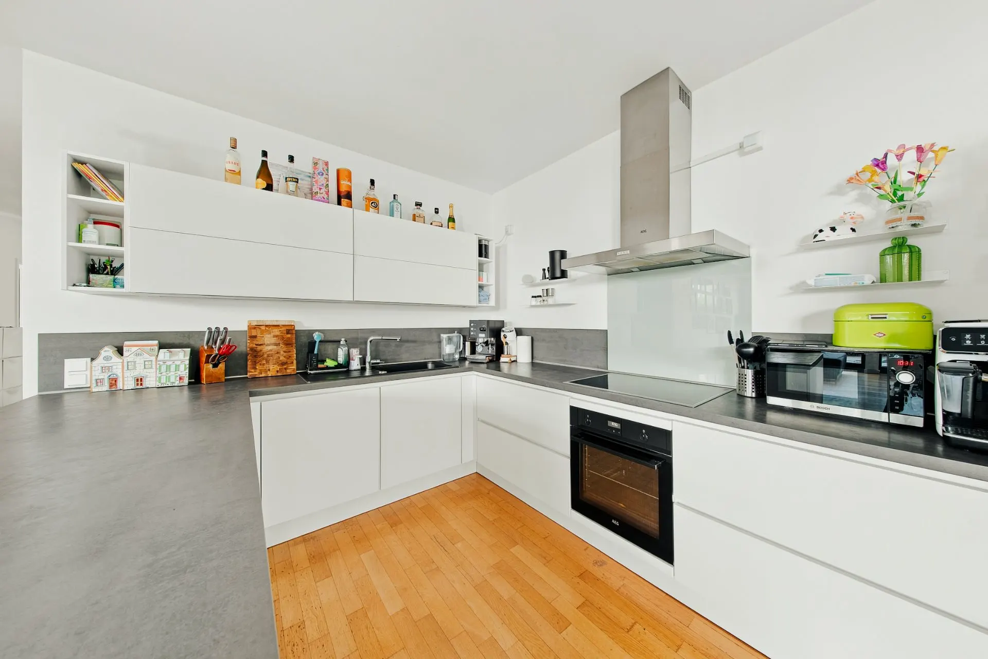 Moderne weiße Einbauküche mit Holzfußboden und diversen Küchengeräten auf der Arbeitsplatte.