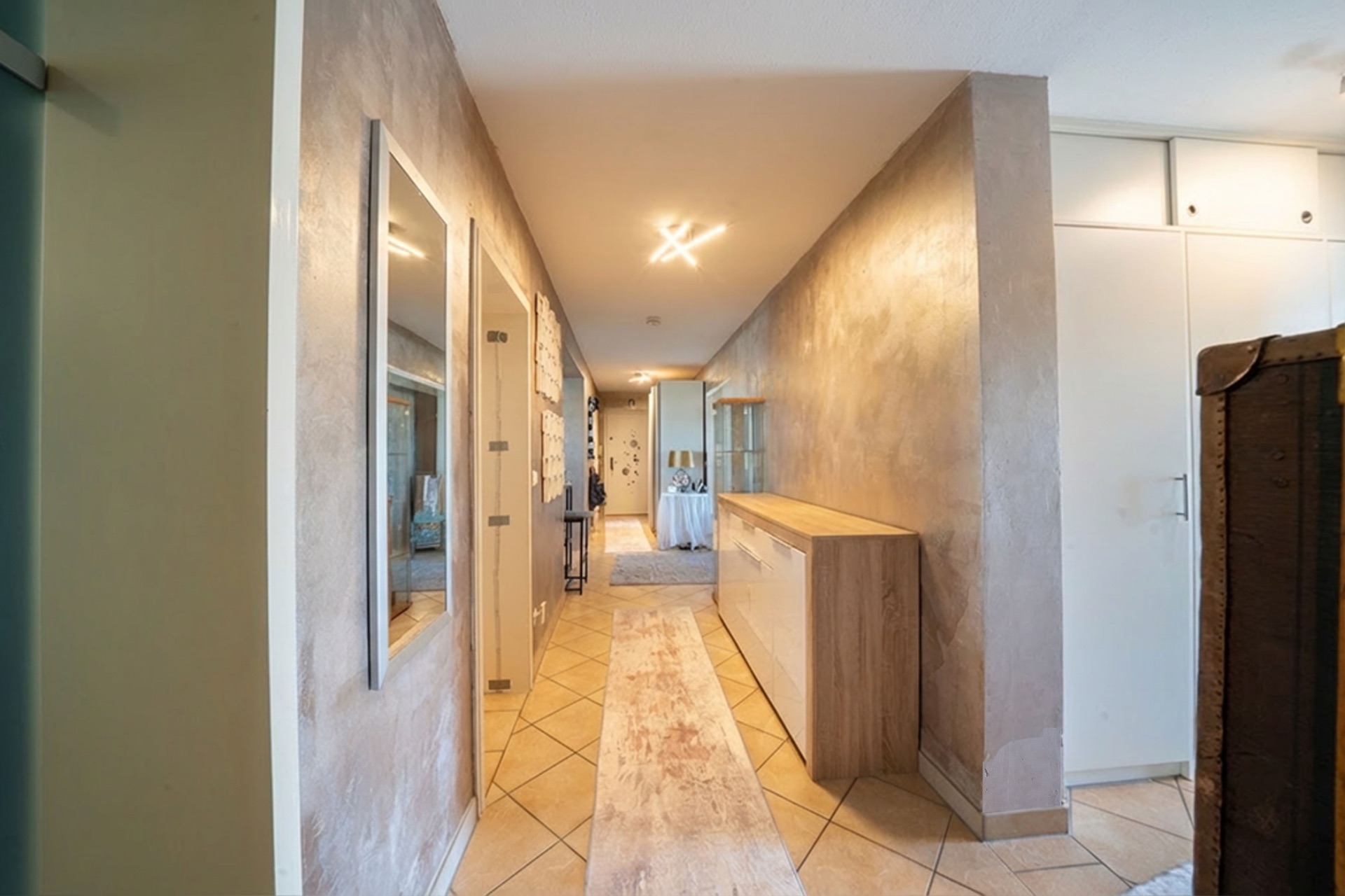 Heller Flur mit Fliesenboden, Spiegeln, Kommode und Einbauschränken in einem Wohnhaus.