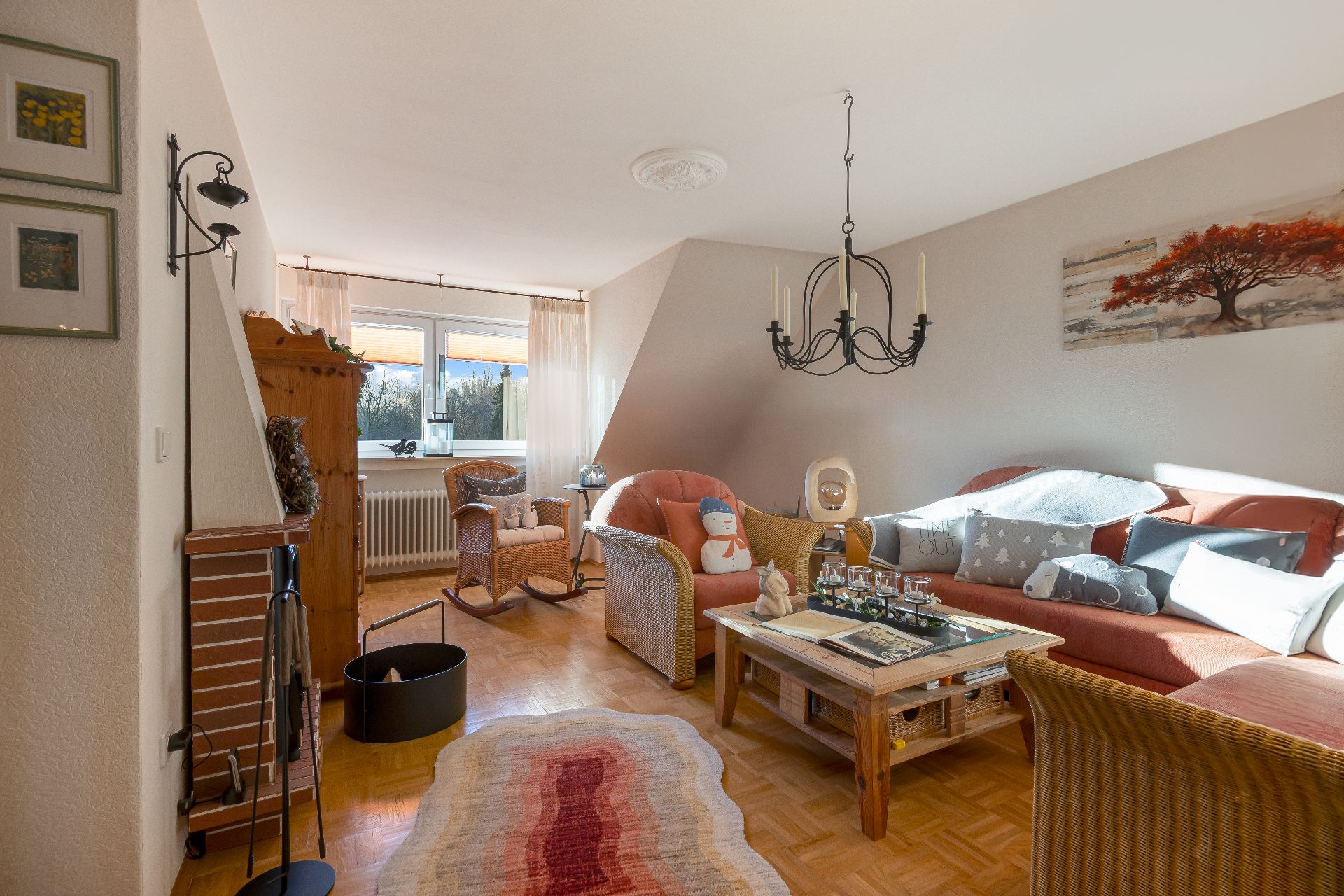 Helles Wohnzimmer mit Korbmöbeln, Kamin, Couchtisch und großen Fenstern.