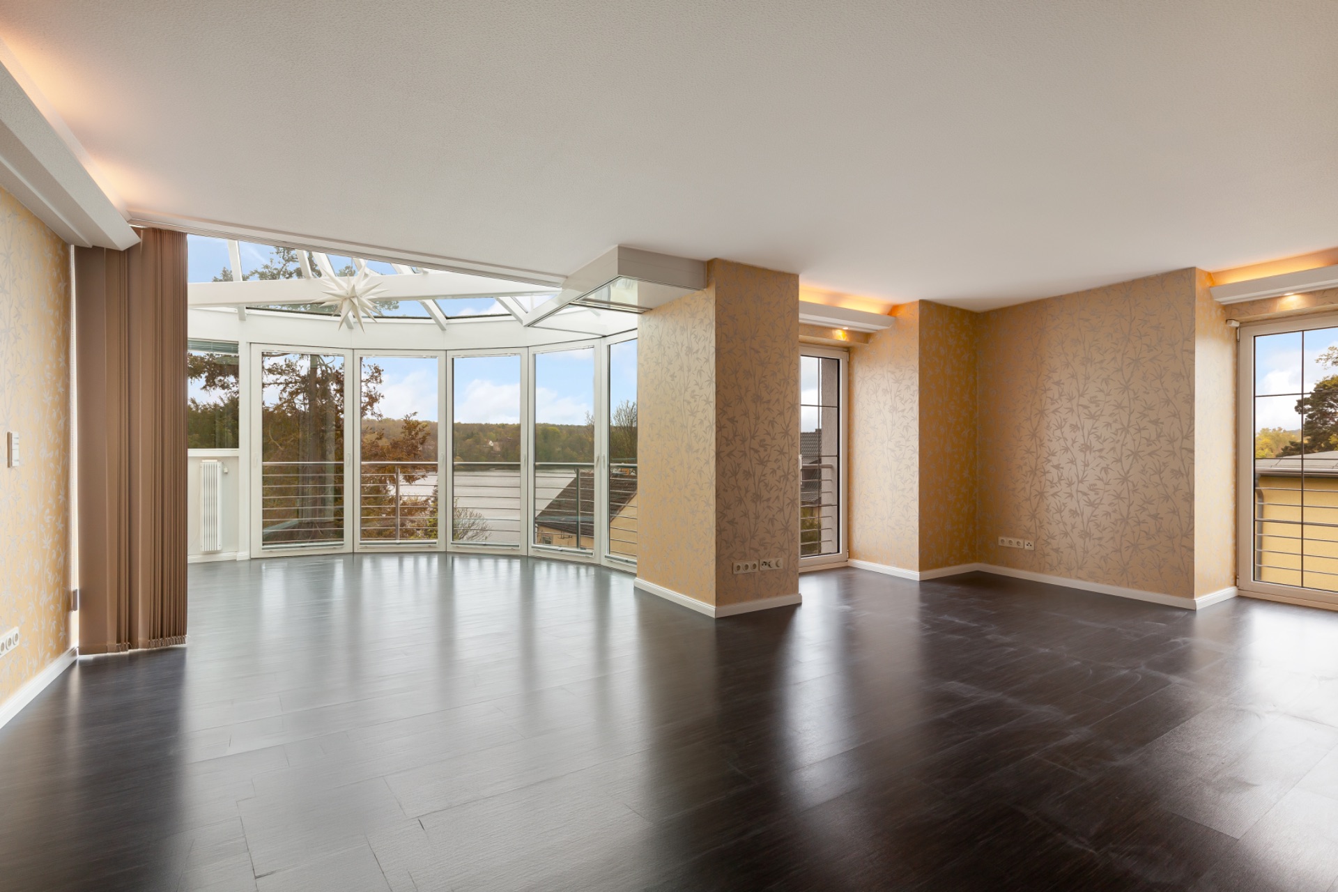 Helles Wohnzimmer mit dunklem Boden, großen Fenstern und Zugang zu einem Balkon.