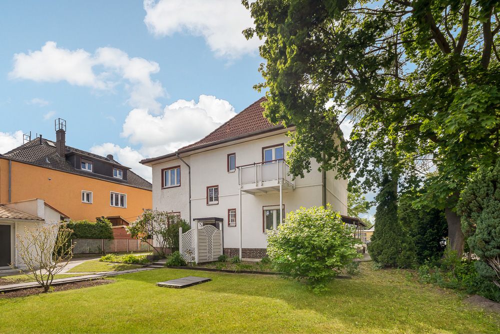 Zweistöckiges Wohnhaus mit Garten, Rasenfläche und mehreren Bäumen im Vordergrund.
