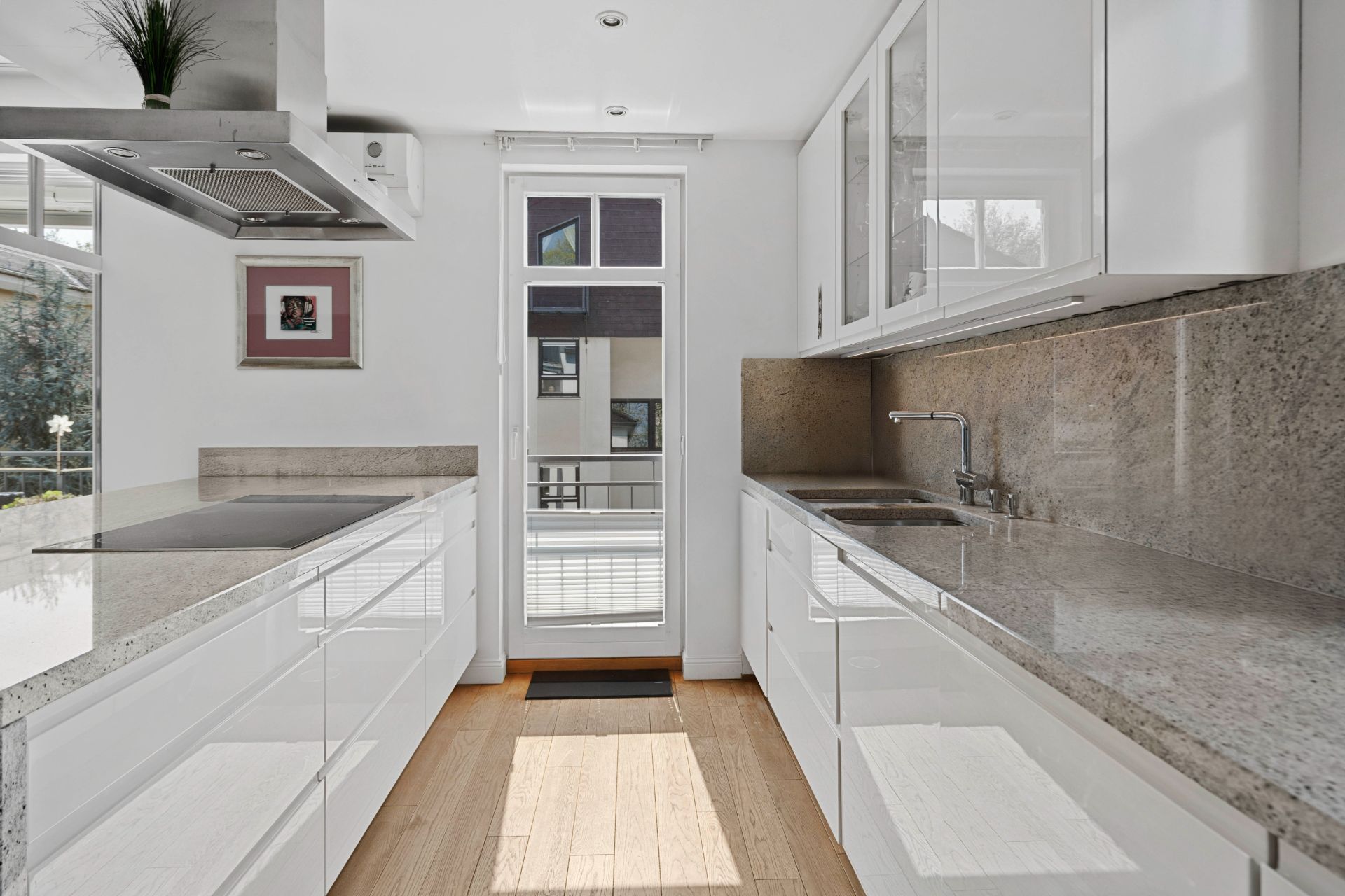 Moderne, helle Küche mit weißen Schränken, Granit-Arbeitsplatten und Zugang zu einem Balkon.