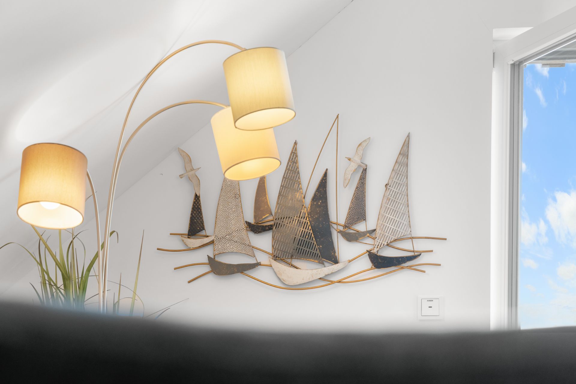 Metall-Wanddeko mit Segelbootmotiven und drei leuchtenden Stehlampen vor weißer Wand.
