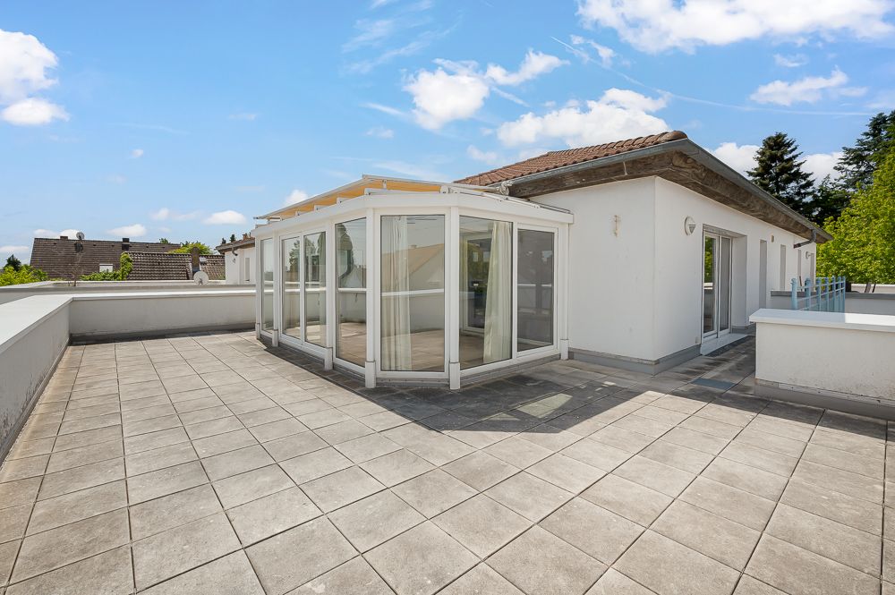 Große Dachterrasse mit Wintergarten an einem weißen Wohnhaus bei sonnigem Wetter.