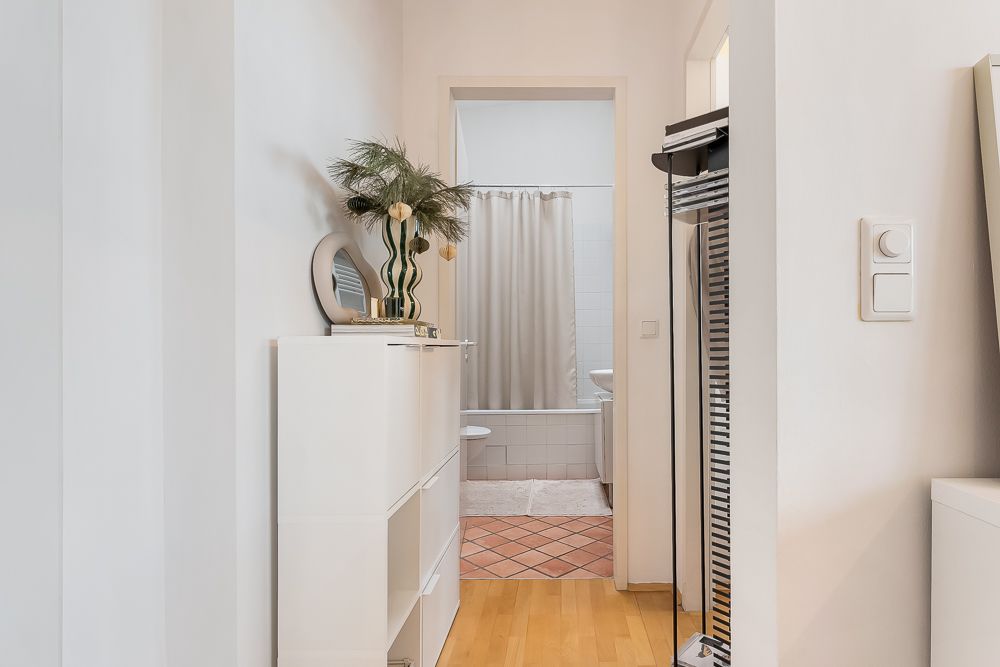 Flur mit weißem Regal, Blick ins Badezimmer mit Badewanne und Duschvorhang.