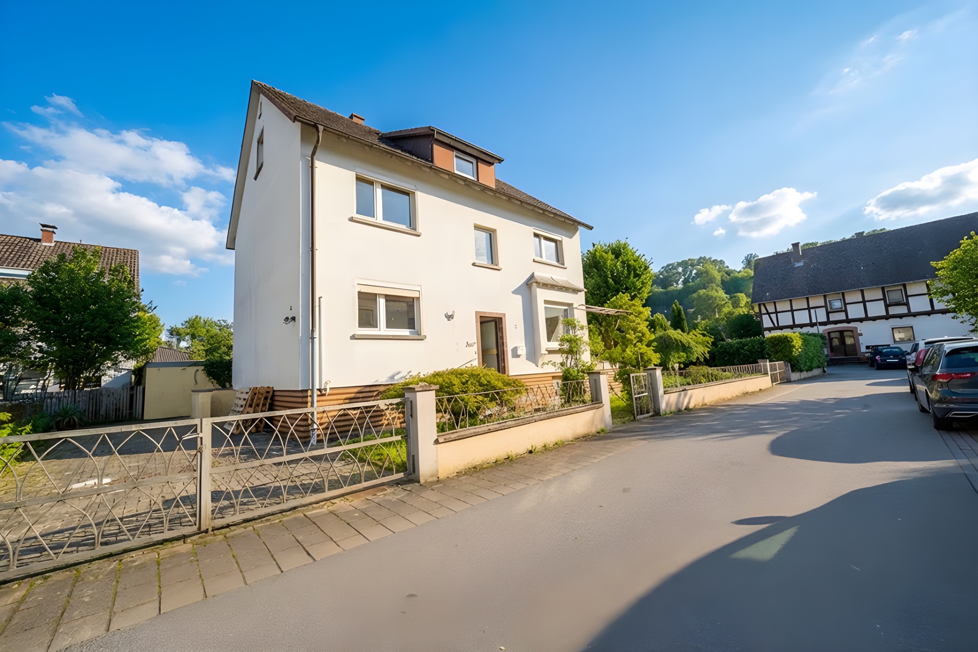 Zweistöckiges weißes Wohnhaus mit Vorgarten und Einfahrt an einer ruhigen Straße.