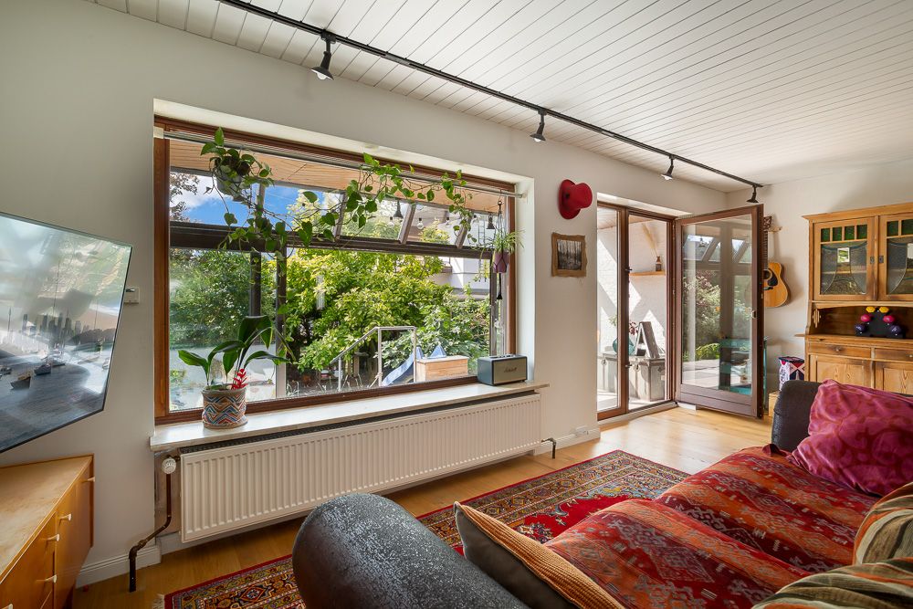 Helles Wohnzimmer mit großem Fenster, rotem Sofa, Holzmöbeln und Zugang zum Garten.