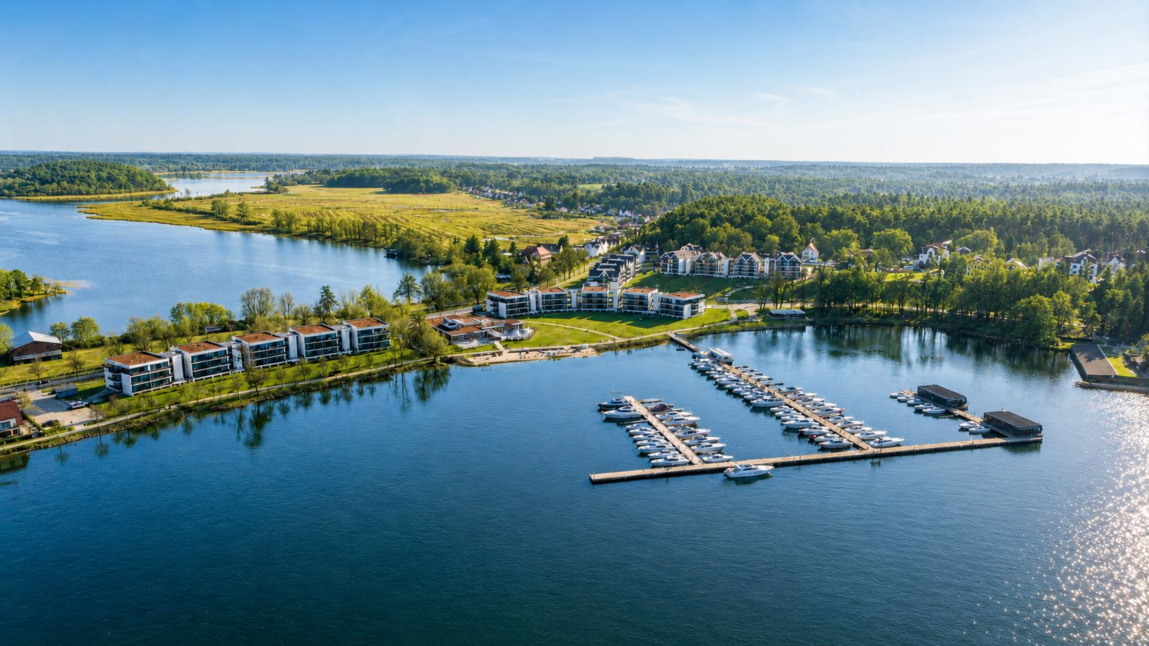 Luftaufnahme von Wohnhäusern am See mit Bootsstegen und umgebender grüner Landschaft.