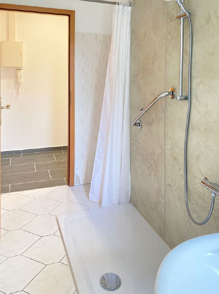 Badezimmer mit begehbarer Dusche, Duschvorhang und Blick in einen Flur.