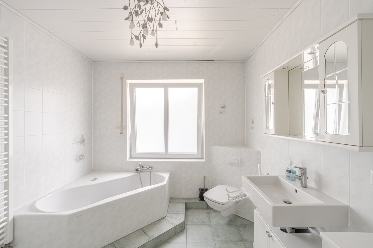 Helles Badezimmer mit Badewanne, Wandtoilette, Waschbecken und großem Fenster.