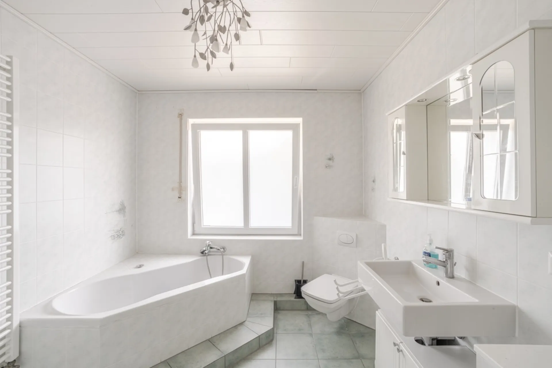 Helles Badezimmer mit Badewanne, Wandtoilette, Waschbecken und großem Fenster.
