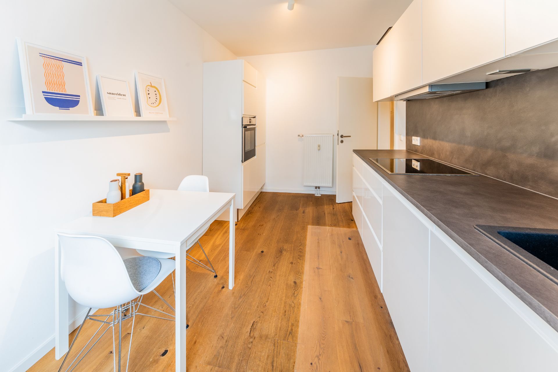 Moderne, helle Küche mit Holzboden, weißem Tisch, Stühlen und Einbauküche.
