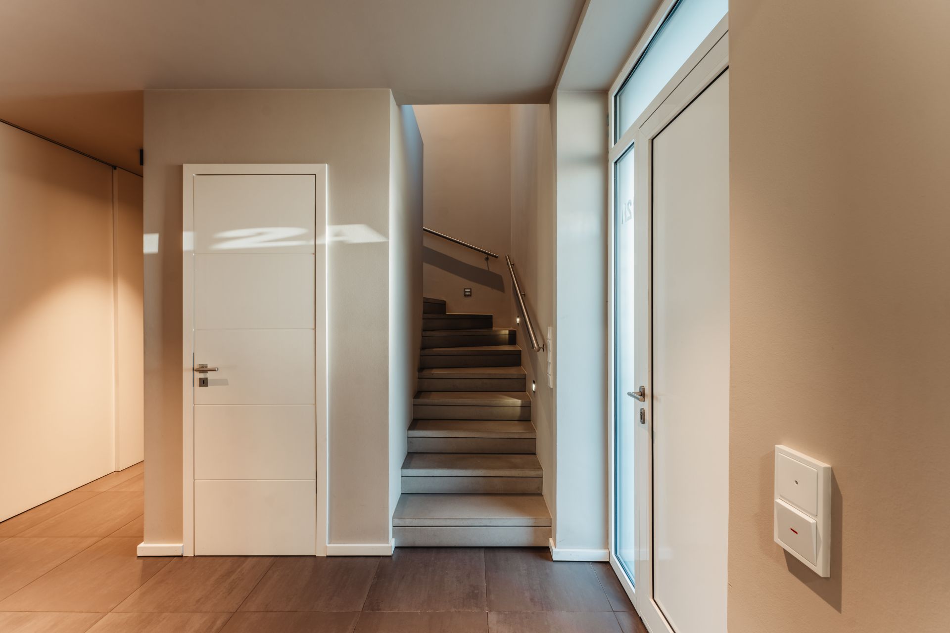 Heller Flur mit zwei weißen Türen und einer Treppe im modernen Wohnhaus.
