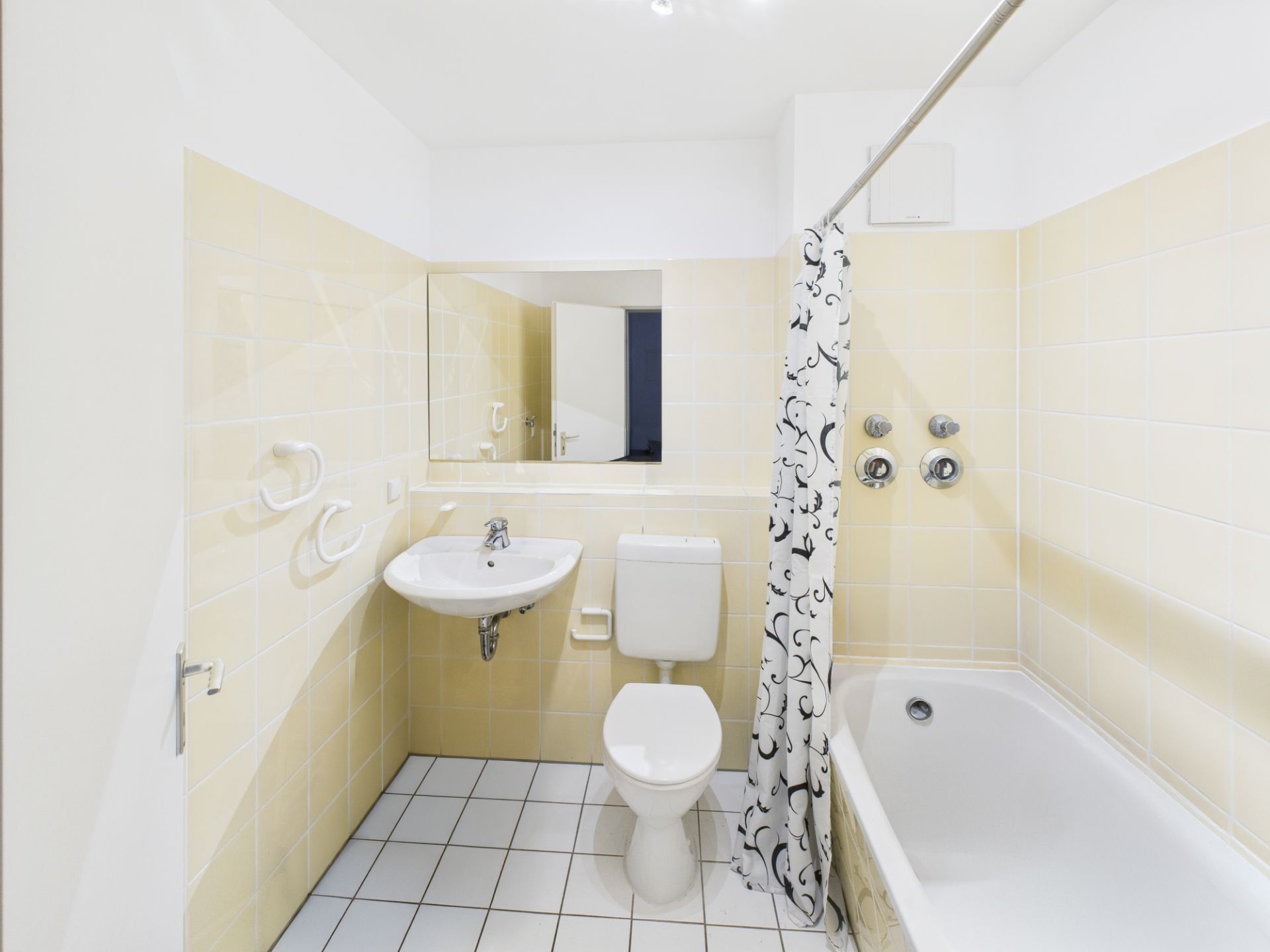 Helles Badezimmer mit Waschbecken, Toilette, Badewanne und Duschvorhang, gelbe Fliesen.